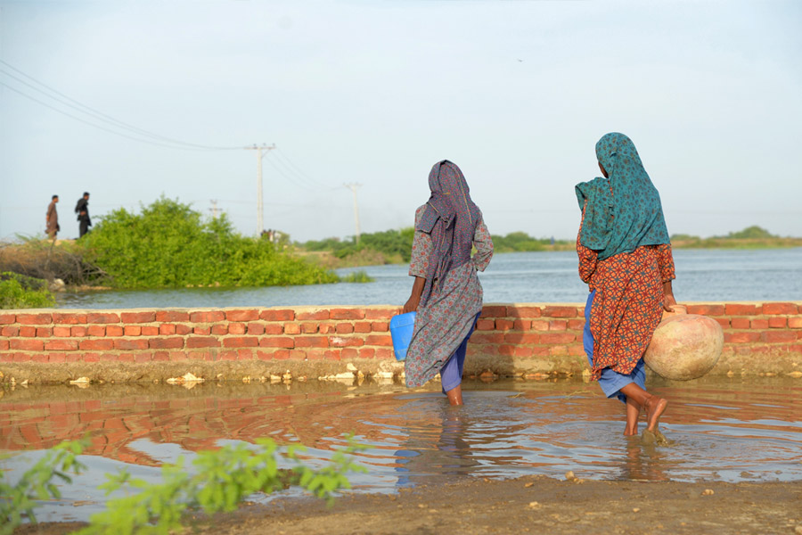 洪水の中を歩くアンシャラ・ビビさん（68歳）（右）（シンド州ジャムショロ地区／パキスタン）Credit: DEC